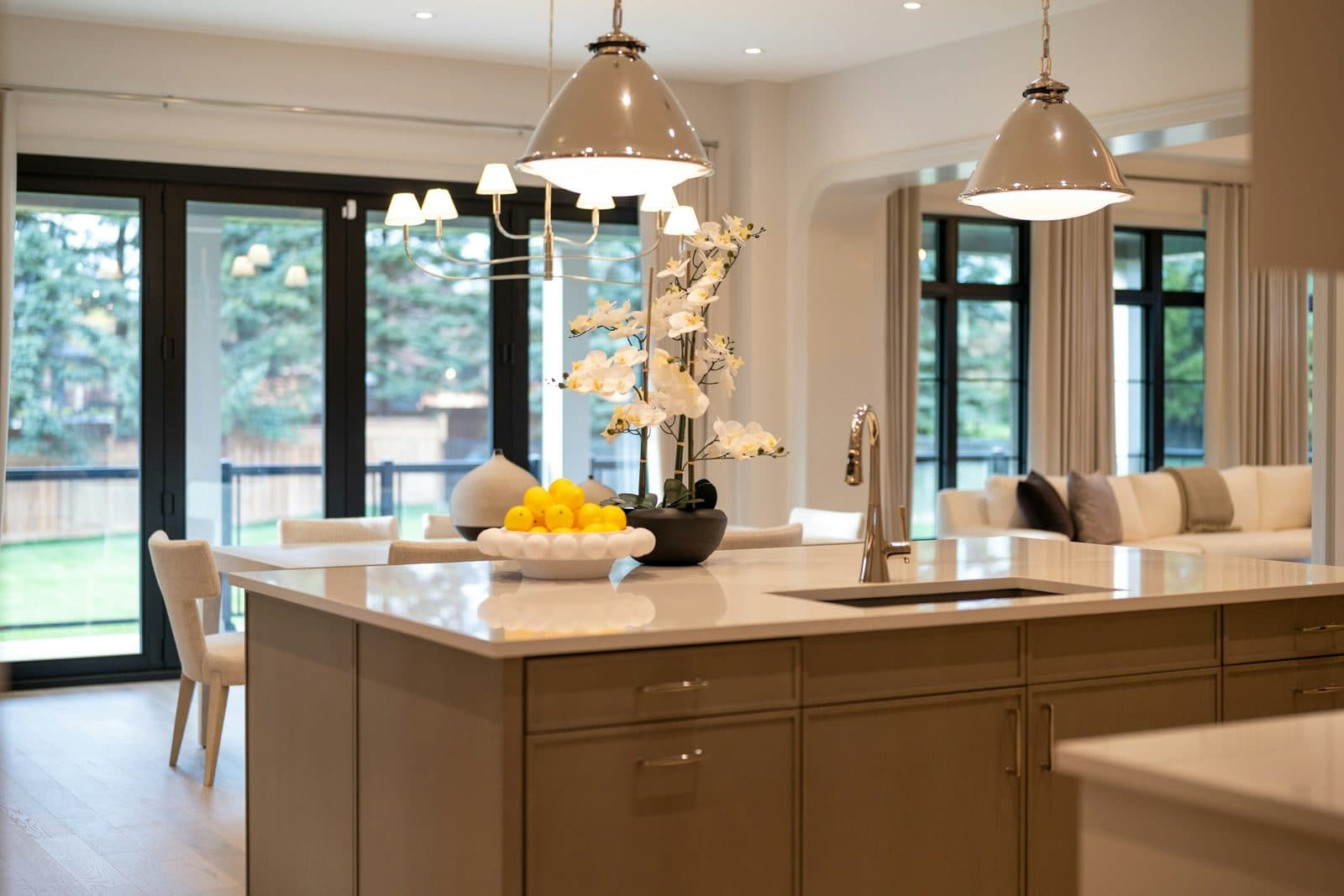 Open kitchen with a marble island, wood cabinets, globe pendants, and a living room beyond